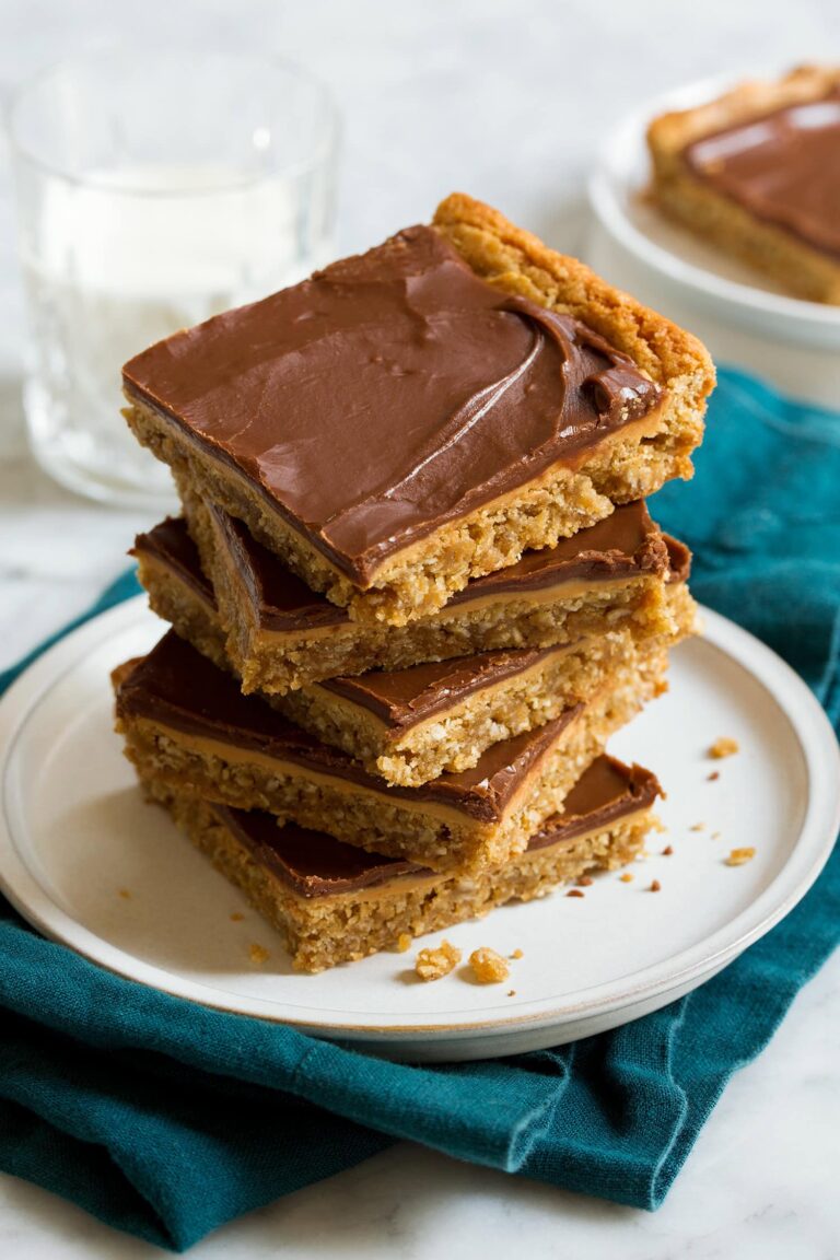 Stack of homemade peanut butter bars with chocolate frosting on a white plate over a teal colored cloth.
