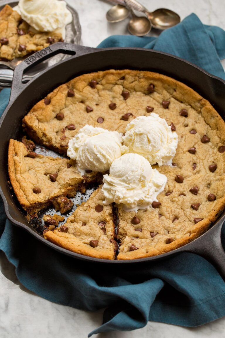 Skillet chocolate chip cookie with two wedges cut and three vanilla ice cream scoops on top.